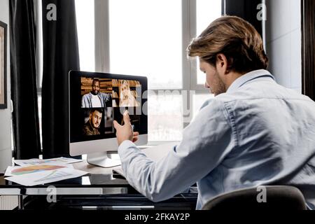 Rückansicht Porträt eines ernsthaften männlichen Mitarbeiters, der bei einem Videomeeting mit Kollegen spricht und am Schreibtisch im Heimbüro sitzt. Ein stilvoller Geschäftsmann ist es Stockfoto