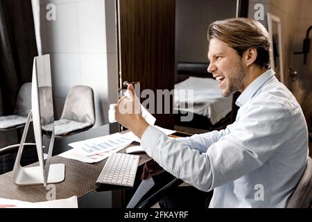 Glücklicher freier Mann, der eine Videokonferenz macht, die Ergebnisse der Teamarbeit genießt und lächelt. Fröhliche stilvolle junge Geschäftsmann kommen, um sich zu einigen Stockfoto