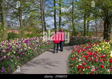 Keukenhof Gardens, Lisse, Niederlande; Paar in passenden roten Anoraks, die durch farbenfrohe Blumenbeete spazieren Stockfoto