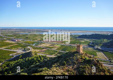 Mediterrane Küstenlandschaft an sonnigen Tagen. Ruinierter Wachturm auf einem Hügel, landwirtschaftliche Felder, Feuchtgebiete in Almenara, Castellon, Spanien Stockfoto