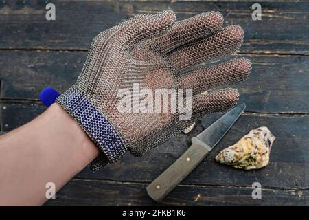 Schutzhandschuhe tragen. Nahaufnahme. Oyster und Messer im Hintergrund Stockfoto