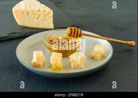 Radamer Käse auf einem Teller serviert mit Honig. Dreieckiges Stück gelbe Kuhmilch schweizer Käse mit Löchern. Stockfoto