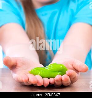 Ein gelber Schleim in den Händen eines Kindes. Ein kleines Kind hält einen Schleim in seinen Handflächen. Spielen Schleim Spielzeug. Stockfoto