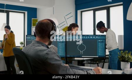 Fokussierter Ingenieur, der Kopfhörer aufsetzt und mit dem technischen cad-Programm arbeitet, Prototypen von 3D-Zahnrädern überprüft, mit Stylus-Bleistift auf dem Grafiktablett zeichnet Industriearchitekt, der die Idee eines Prototyps am pc studiert Stockfoto