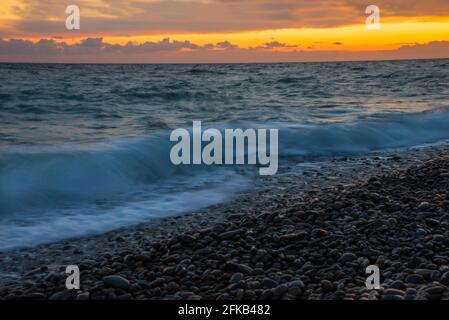 Leuchtender gelb-oranger Sonnenuntergang am Meeresstrand. Kiesstrand an der Schwarzmeerküste Stockfoto