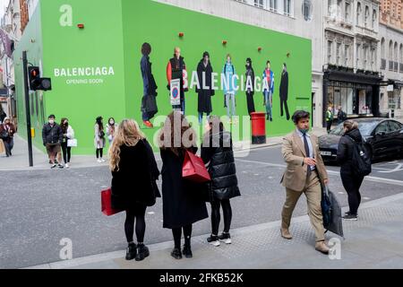 Die Käufer überqueren die Straße in Richtung des temporären Hortens für Balenciaga, ein Einzelhandelsgeschäft, das am 27. April 2021 in der Bond Street in London, England, eröffnet wird. Balenciaga ist ein Modehaus, das 1917 vom spanischen Designer Cristóbal Balenciaga in San Sebastián, Spanien, gegründet wurde. Stockfoto