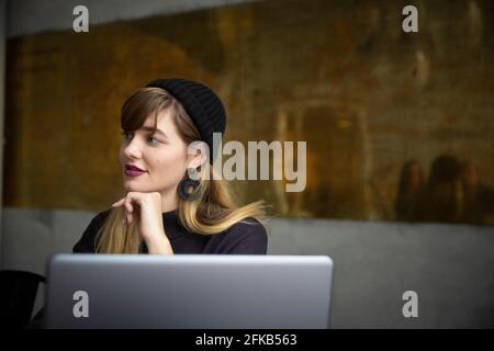 Lächelnde Geschäftsfrau mit der Hand am Kinn am Laptop im Büro Stockfoto