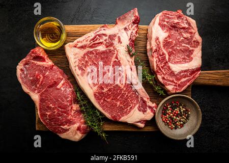 Vielfalt an frischen Raw Black Angus Prime Meat Steaks T-bone, New York, Ribeye und Gewürzen auf schwarzem Hintergrund, Draufsicht Stockfoto