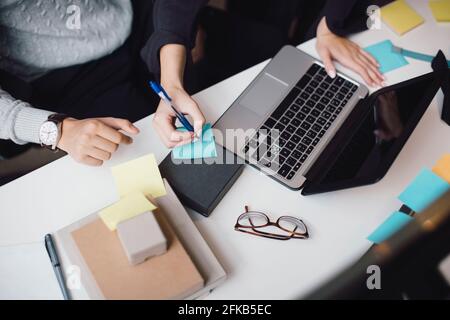 Kurze Hand einer Geschäftsfrau, die per Laptop auf eine Haftnotiz schreibt Am Schreibtisch im Büro Stockfoto