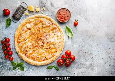 Leckere Pizza mit Hühnchen und süßer und saurer Sauce und Kochzutaten Tomaten und Basilikum auf hellblauem Hintergrund. Draufsicht Stockfoto