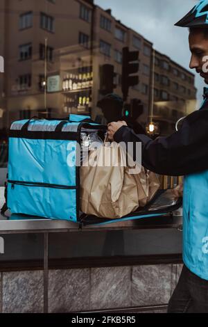 Zugeschnittenes Bild des Lieferers, der die Paketbestellung in den Rucksack legt Außerhalb des Ladens Stockfoto