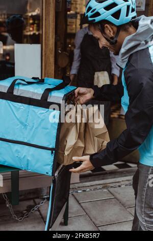 Lieferung Mann Putting Paket bestellen im Rucksack vor Delikatessengeschäft Stockfoto