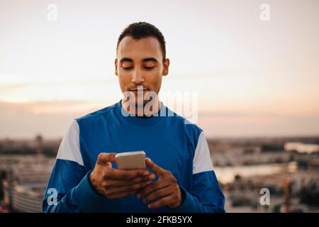 Sportler, die während des Sonnenuntergangs Smartphone gegen den Himmel benutzen Stockfoto