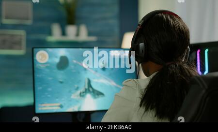Nahaufnahme von wettbewerbsfähigen schwarzen Frau Spieler mit Joystick spielen Weltraum-Shooter-Videospiel auf leistungsstarken Computer spät in der Nacht. Professioneller Gamer mit Wireless-Controller für Online-Gaming-Meisterschaft Stockfoto