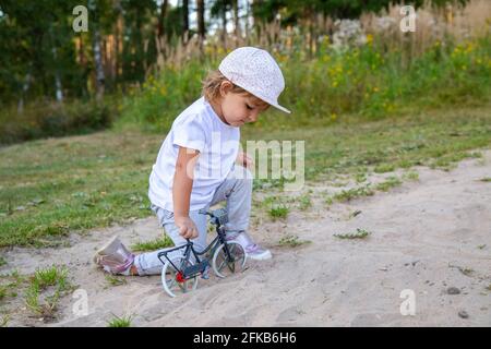 Liebenswert Kleinkind spielt mit einem Spielzeug Fahrrad in der Natur. Kind auf allen Vieren im Sand auf dem Rasen. Stockfoto