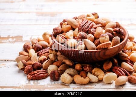 Gemischte Nüsse in Holzschüssel und auf dem Tisch verstreut. Trail Mischung aus Pecan, Mandel, Macadamia & brasilien essbare Nüsse mit Walnuss Haselnuss auf Holz strukturiert sur Stockfoto