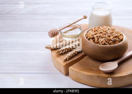 Eine Holzschale mit einer Mischung aus Mandeln, Rosinen, Samen, Cashew, Haselnüssen, Glas Milch und Honig auf weißem Tisch. Vegetarische Ernährung Sport Nutr Stockfoto