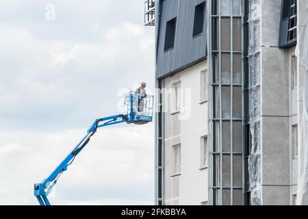 Weißrussland, Minsk - 28. Mai 2020: Industriearbeiter auf der Hebebühne in der Nähe der neuen Fassade des Hauses, das auf der Baustelle im Bau ist. Stockfoto