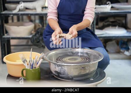 Kurzer Schuss einer Frau in blauer Schürze, die handgefertigten Ton erzeugt Keramik in Töpferwerkstatt Studio Stockfoto