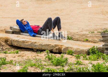 Weißrussland, Minsk - 28. Mai 2020: Junger Arbeiter in einer Pause, der auf einer Baustelle auf einer alten Betonplatte schläft. Stockfoto