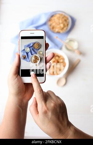 Junge Frau Food-Bloggerin macht Foto für Blog, Bild von Schüssel mit griechischem Joghurt hausgemachtes Müsli, gemischte Nüsse, Mandel, Cashew, Haselnuss. Gesunde Vegetaria Stockfoto