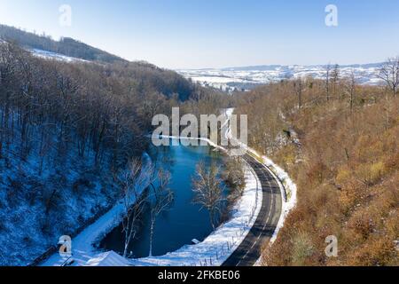 Drohnenaufnahme eines gefrorenen Sees von oben durch eine vorbeifahrende Straße im Wald. Stockfoto