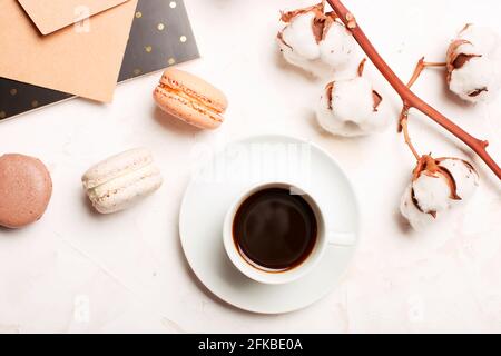 Stilvolle Zusammensetzung, Französisch sortierte Schokolade Makronen, Kaffeetasse, Notizbuch, Baumwolle boll, weißen Stuckputz strukturierte Tisch. Alles gute zum Geburtstag mothe Stockfoto