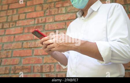 Geschäftsmann in Gesichtsmaske stehend und mit seinem Handy für Messaging. Konzentrieren Sie sich auf Finger und Telefon. Stockfoto