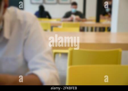 Menschen mit Gesichtsmaske sitzen und lesen auf dem Tisch in der Bibliothek. Unschärfe-Unschärfe. Stockfoto