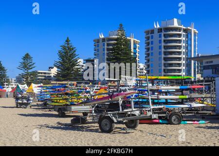 Surfboote auf Anhängern an einem sonnigen Strand, mit Hochhäusern im Hintergrund. Mount Maunganui, Neuseeland Stockfoto