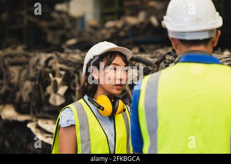 asiatische Ingenieurin, die Frauen arbeitet, die mit jungen Männern zusammenarbeiten Mann am Arbeitsplatz in der Schwerindustrie, der Helm-Schutzanzug waring Stockfoto