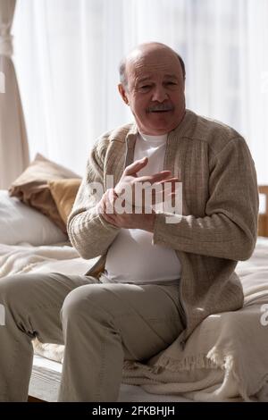 Mann mit Schmerzen im Handgelenk sitzt zu Hause auf dem Bett und leidet an Rheuma Stockfoto