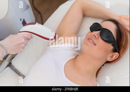 Arzt, der im Salon Laserhaarentfernung auf der Achselhöhle einer Frau macht. Eine alternative Möglichkeit, unerwünschte Körperhaare dauerhaft zu entfernen Stockfoto