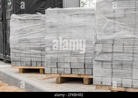 Ein Stapel neuer Pflasterplatten auf einer Holzpalette, die in Plastikfolie eingewickelt ist. Baustoffe auf der Baustelle. Stockfoto