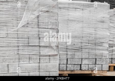 Ein Stapel neuer Pflasterplatten auf einer Holzpalette, die in Plastikfolie eingewickelt ist. Baustoffe auf der Baustelle. Stockfoto