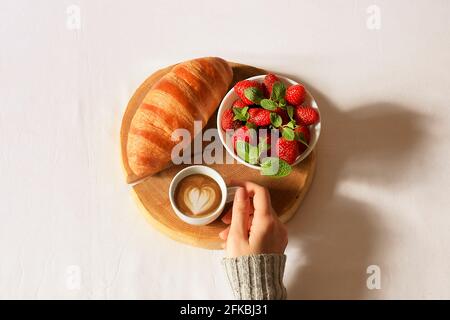 Über dem Kopf geschnittene Aufnahme einer Frau, die ein Mittagessen mit Croissants und Kaffee hatte und ihr Telefon scrollte. POV. Stockfoto