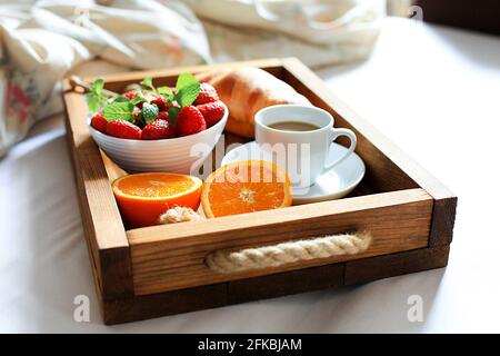 Frühstück auf einem Tablett mit einer Tasse Kaffee, frischen französischen Croissants und Obst auf weißem Laken von oben, Kopierplatz. Flitterwochen. Morgen im Hotel. Stockfoto