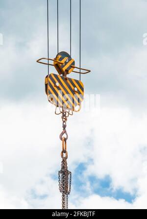 Das Heben der schweren Ausrüstung der Hebemechanismus des Turmkrans mit dem Haken und der Kette gegen den Himmel. Nahaufnahme. Stockfoto