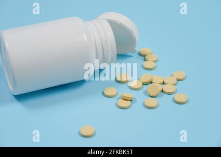 Weiße Pillen, die aus einer gestürzten weißen Pillenflasche verschüttet werden. Isoliert auf blauem Hintergrund. Medizinkonzept Stockfoto