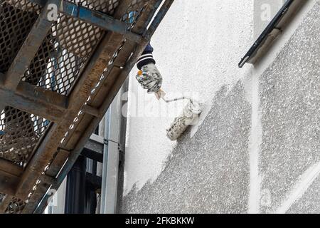 Ein Industriearbeiter auf einer Hebebühne malt die Fassade eines neuen modernen Stadtgebäudes, das auf einer Baustelle im Bau ist. Stockfoto