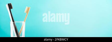 Umweltfreundliche natürliche Bambus-Zahnbürste und zwei Kunststoff-Zahnbürsten in einem Glas auf blauem Hintergrund. Gesundheitswesen, Kopierbereich. Stockfoto