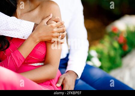 Braut und Bräutigam sitzen nebeneinander, der Bräutigam umarmt die Braut an den Schultern, die Braut legt ihre Hand auf die Hand des Bräutigams Stockfoto