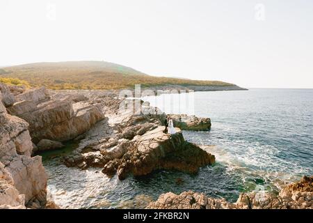 Die Braut und der Bräutigam stehen mit den Händen auf den Felsen Am Meer und einander anschauen Stockfoto