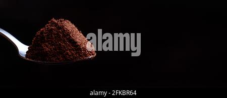 Ein atemberaubendes Foto von gemahlenem Kaffee in einem Löffel auf schwarzem Hintergrund. Banner mit Platz für Text für Werbung oder Angebot eines Cafés. Stockfoto