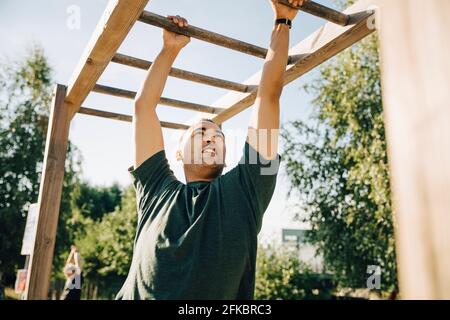 Männlicher Athlet, der an der Affenbar im Park bei Sonnenschein hängt Tag Stockfoto