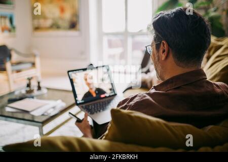 Reifer Geschäftsmann auf Videoanruf mit männlichem Kollegen im Leben Raum während einer Pandemie Stockfoto