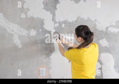 Eine Bauherrin entfernt alte Tapeten von der Wand. Schlüsselreparaturen, Banner mit Platz für Text. Stockfoto