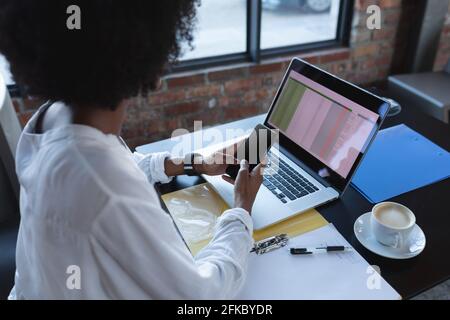 afroamerikanische Frau, die mit Smartphone und Laptop im Café sitzt Stockfoto