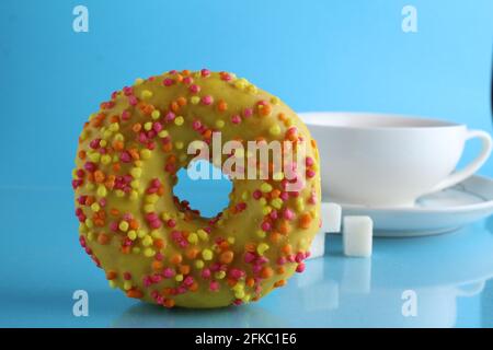 Stillleben Donuts gelb rosa gelbe Schokolade und eine Tasse Tee-Kaffee im Hintergrund auf einem blauen hellen Hintergrund. Ein Tag ohne Diäten. Poster zu t Stockfoto