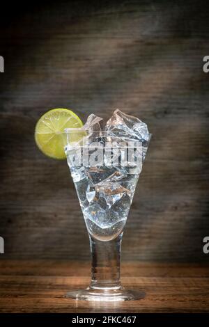 Glas Eiswasser mit einer Scheibe Kalk auf einer hölzernen Tischplatte mit Sonnenstrahlen. Stockfoto